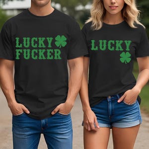 May include: Black t-shirts with green text and shamrock designs. One shirt reads "LUCKY FUCKER", the other reads "LUCKY". Both shirts are paired with blue denim bottoms. The shirts are likely for St. Patrick's Day.