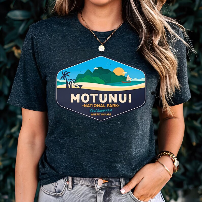 May include: Dark grey t-shirt with a colourful graphic of a coastal scene, including the text "MOTUNUI NATIONAL PARK". The design features a mountain, sun, and sailboat. The shirt also has the text "Find happiness where you are".