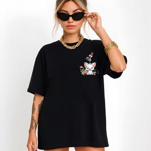 May include: Black t-shirt featuring a colorful graphic of a pig, rooster, and flowers. The design is on the left chest area. The shirt has short sleeves and a relaxed fit.