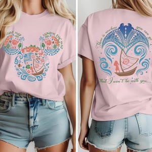 May include: Pink t-shirt featuring a Mickey Mouse-shaped design with floral and boat illustrations, and the text "WHAT MAY I KNOW THE WAY". The back of the shirt has a boat illustration and the text "There is nowhere you can go that I won't be with you..."