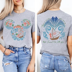 May include: A gray t-shirt featuring a colorful design inspired by a popular animated film. The front design includes a Mickey Mouse head shape filled with floral and nautical elements, with the text "COME WHAT MAY" and "I KNOW THE WAY". The back of the shirt has a boat design with the text "There is nowhere you can go that I won't be with you..."