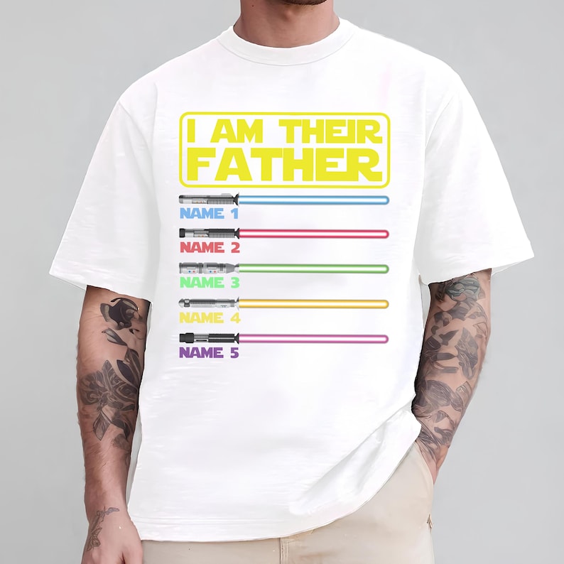 May include: White t-shirt with the text "I AM THEIR FATHER" in yellow. Below the text are five lightsabers with different colored blades and the text "NAME" followed by a number. The shirt is a crew neck.