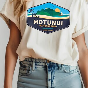 May include: Off-white t-shirt with a vibrant graphic depicting a tropical island landscape. The design includes the text "MOTUNUI NATIONAL PARK. Find happiness WHERE YOU ARE", palm trees, mountains, and a setting sun.