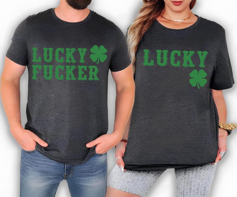 May include: Two dark gray t-shirts with green text and a green shamrock. One shirt says "LUCKY FUCKER" and the other says "LUCKY". The shirts are short-sleeved and appear to be made of a soft material.
