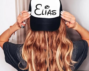 May include: Black and white trucker hat with the name "ELIAS" written in a stylized font on the front.