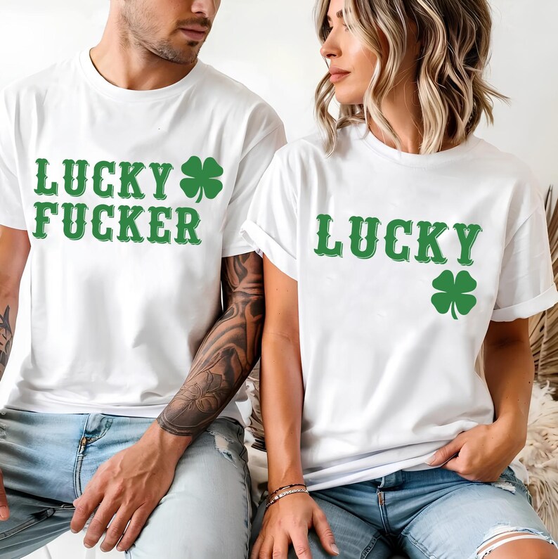 May include: White t-shirts with green text and shamrock graphics. One shirt reads "LUCKY FUCKER" and the other says "LUCKY". Both shirts are paired with blue jeans. The shirts are likely for St. Patrick's Day.