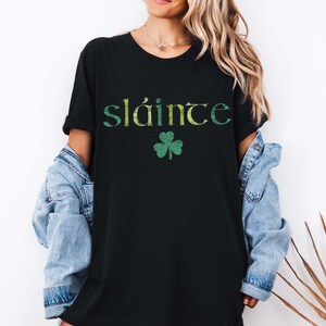 May include: Black t-shirt with the word "sl&aacute;inte" in green and yellow lettering and a green shamrock graphic. The shirt is a casual style, suitable for St. Patrick's Day or Irish heritage events.
