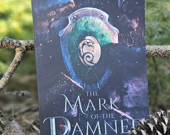 May include: A book cover with a dark background and a green and blue shield with a silver crest. The title is "The Mark of the Damned" and the subtitle is "The Vorelian Saga Book 1".