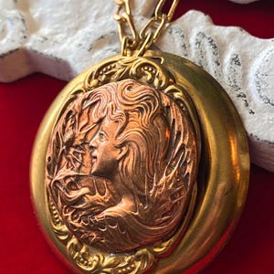 May include: A vintage gold-tone pendant necklace. The pendant features a copper-toned relief of a woman's profile surrounded by floral and leaf details. The necklace has a gold chain and a round, ornate frame.
