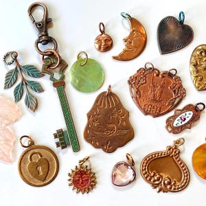 Könnte beinhalten: Eine Sammlung von 16 Vintage-Anhängern, darunter ein Schlüssel, ein Vorhängeschloss, eine Mondsichel, ein Herz, eine Sonne, ein Blatt und ein Vogel. Die Anhänger sind aus Metall und haben verschiedene Oberflächen, darunter Gold, Silber und Kupfer.