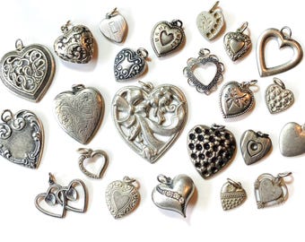 May include: A collection of silver charm pendants in the shape of hearts. The charms feature various designs, including a heart with a bow, a heart with a floral pattern, and a heart with a simple outline.