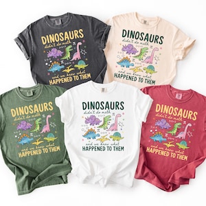 five t-shirts with dinosaur designs and text, arranged in a row.