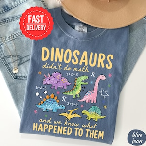 A blue t-shirt with a cartoon dinosaur design and text, along with a red "FAST DELIVERY" sticker and a "Comfort Colors" label.