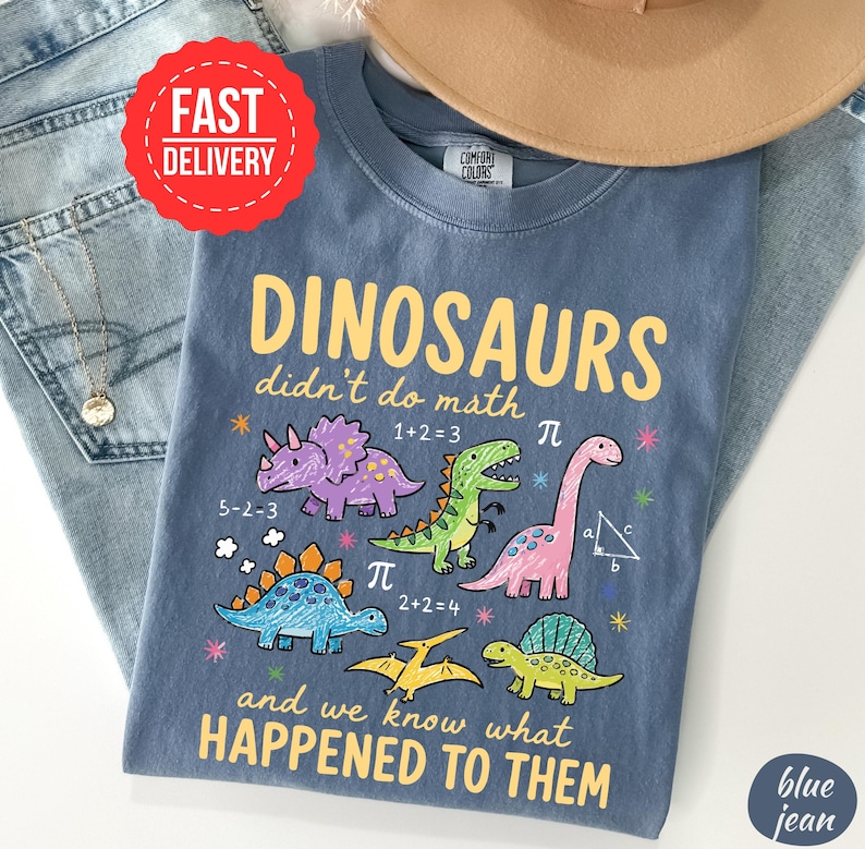 A blue t-shirt with a cartoon dinosaur design and text, along with a red "FAST DELIVERY" sticker and a "Comfort Colors" label.