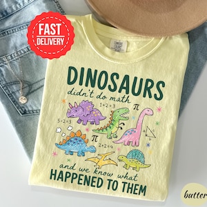 A yellow t-shirt with a cartoon dinosaur design and text, along with a pair of jeans and a hat, suggesting a casual outfit.