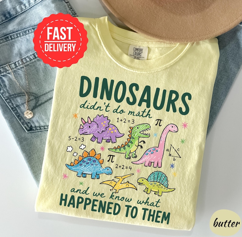 A yellow t-shirt with a cartoon dinosaur design and text, along with a pair of jeans and a hat, suggesting a casual outfit.