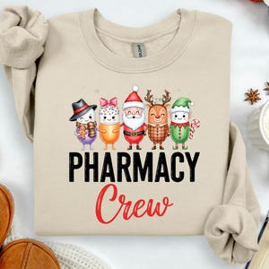 May include: A sand-coloured sweatshirt with a graphic of five cartoon characters in festive outfits. The text "PHARMACY Crew" is printed in black and red. The sweatshirt has long sleeves and a crew neck.