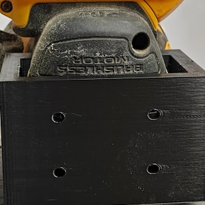 Op de afbeelding: Een gele en zwarte DeWalt 20V accuschuurmachine met een zwart opzetstuk. Op de schuurmachine staat de tekst "DEWALT" en "BRUSHLESS MOTOR". Het opzetstuk heeft vier gaten.
