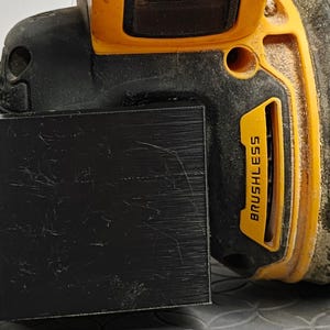Op de afbeelding: Close-up van een zwart en geel draadloos elektrisch gereedschap. De tool heeft een zwarte basis met een gele bovenkant en een zwart rechthoekig opzetstuk. De woorden "BRUSHLESS" staan op de zijkant.