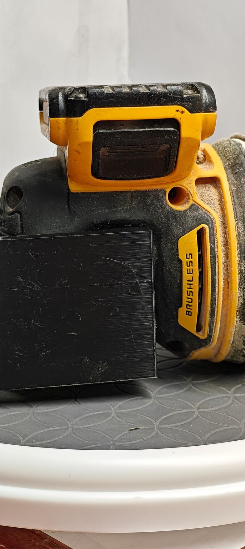 Op de afbeelding: Close-up van een zwart en geel draadloos elektrisch gereedschap. De tool heeft een zwarte basis met een gele bovenkant en een zwart rechthoekig opzetstuk. De woorden "BRUSHLESS" staan op de zijkant.