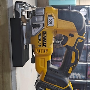 May include: A yellow and black DeWalt 20V XR cordless jigsaw mounted on a wall. The tool features a black handle and base with the DeWalt logo and model information visible. The jigsaw is attached to a black mounting bracket.