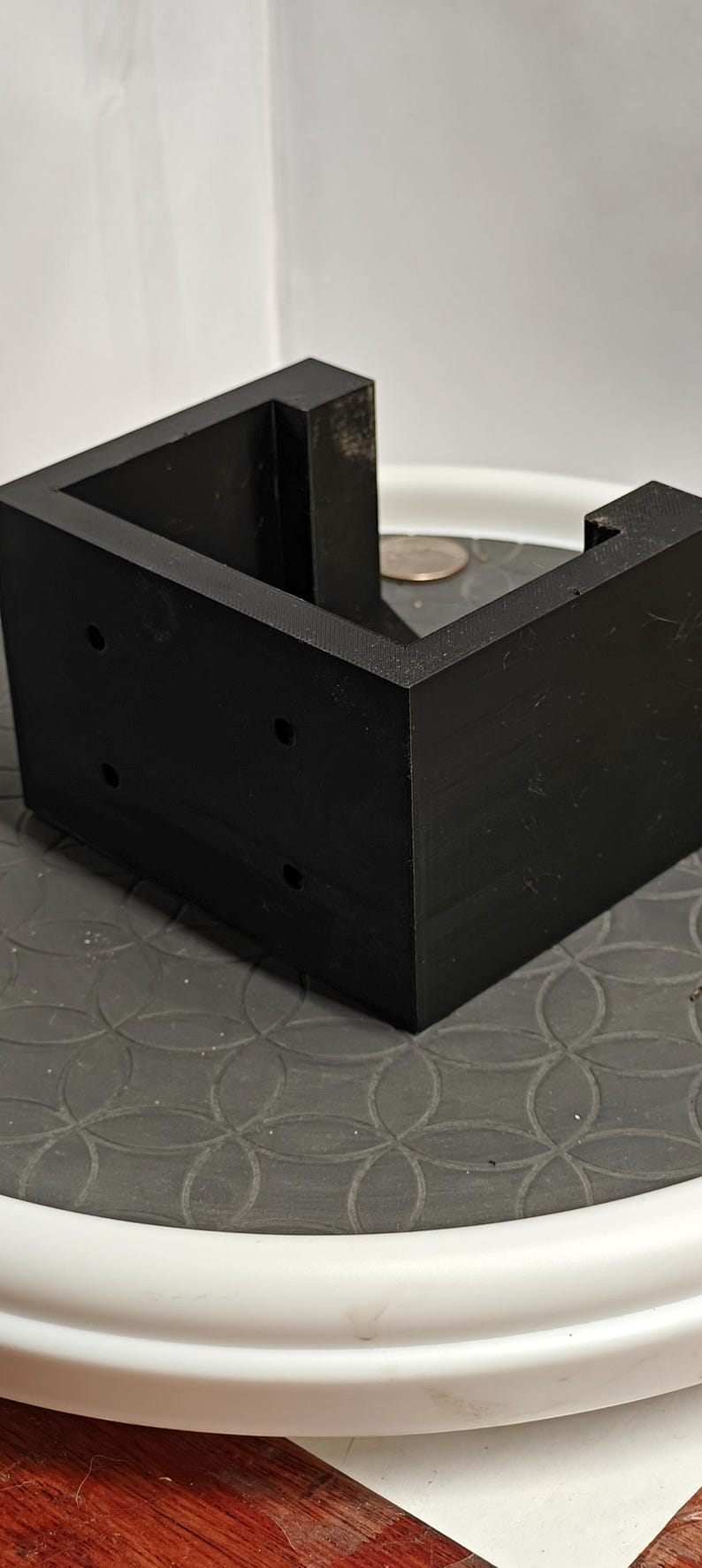 Op de afbeelding: Een zwart, L-vormig object met drie kleine gaten aan &eacute;&eacute;n kant. Het object is gemaakt van een massief materiaal en staat op een patroon. Het object lijkt een hoekbeugel of steun te zijn.