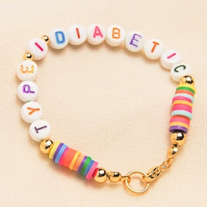 May include: A colourful beaded bracelet spelling "DIABETIC TYPE". The bracelet has white letter beads, gold-coloured accents, and a clasp. It also features colourful disc beads.