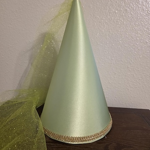 May include: A light green satin cone-shaped hat with a gold trim at the base. A matching green, glittery tulle veil is attached to the hat. The hat is likely for a costume or special occasion.