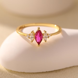 Peut inclure: Une bague en or avec une pierre précieuse rose en forme de marquise entourée de petites pierres précieuses claires.
