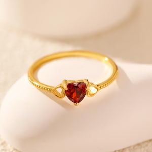 Peut inclure: Une bague en or avec une pierre précieuse rouge en forme de cœur et deux découpes en forme de cœur plus petites de chaque côté de la pierre.