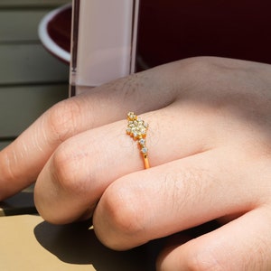 May include: A gold ring with a cluster of small white stones set in a delicate floral design.