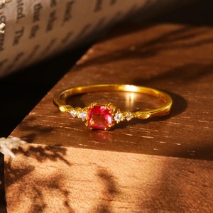 May include: A gold ring with a red gemstone and small white gemstones set in the band.
