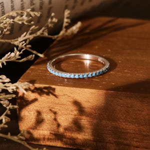 May include: A silver band ring with a row of light blue turquoise stones.
