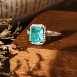 May include: A silver ring with a large, emerald-cut turquoise gemstone surrounded by a halo of smaller diamonds.