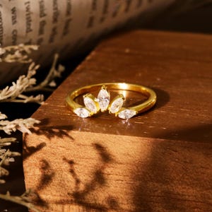 Può includere: Un anello d'oro con una fila di pietre chiare a forma di marquise incastonate in una fascia curva.