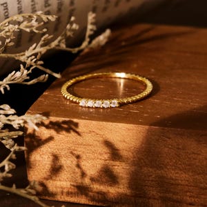 May include: A delicate gold ring with a textured band and five small clear stones set in a row.