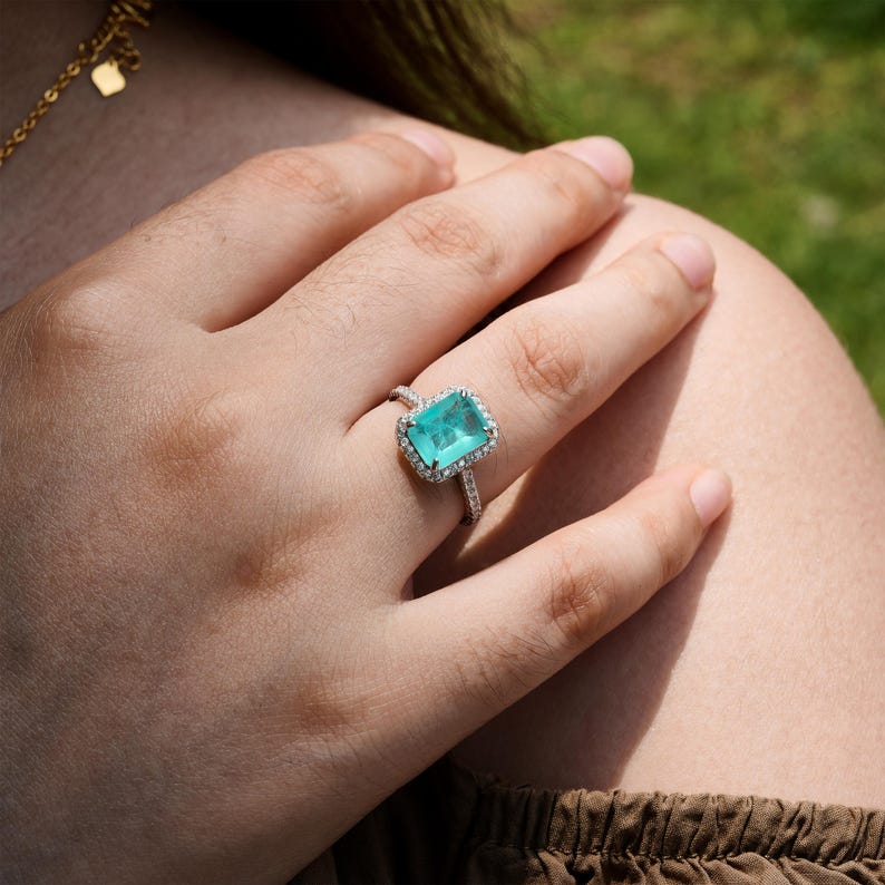 May include: A silver ring with a large, rectangular, light blue gemstone surrounded by smaller, clear gemstones.