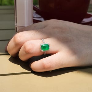 May include: A silver ring with a large emerald green gemstone surrounded by smaller diamonds.