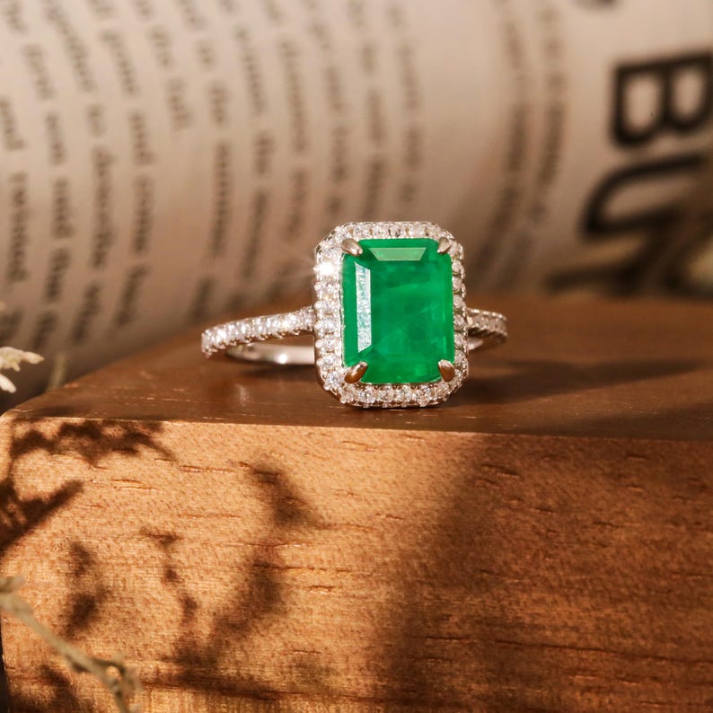 May include: A silver ring with a large emerald green gemstone surrounded by a halo of smaller diamonds.