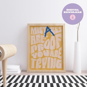 May include: A yellow and white framed print with the text "Mistakes are proof you are trying" in a retro font. The text is in a light pink color with a blue "A" in the word "Mistakes".