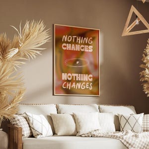 Puede incluir: Un cuadro enmarcado con la frase "NOTHING CHANGES IF NOTHING CHANGES" en una fuente retro. La obra de arte tiene una paleta de colores cálidos de naranja, rosa y amarillo. El cuadro cuelga sobre un sofá con cojines decorativos.
