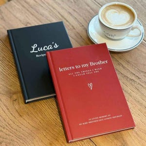 two books titled "Lucas's Recipe" and "Letters to my Brother" placed on a wooden table, with a cup of coffee nearby.