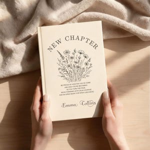 May include: A cream-coloured book titled "New Chapter" with floral illustrations and inspirational text. The book's cover features the author's name, Emma Collins. The book is held by a person.