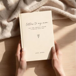 A person's hands holding a book titled "Letters to my mom" with a heart symbol on the cover.