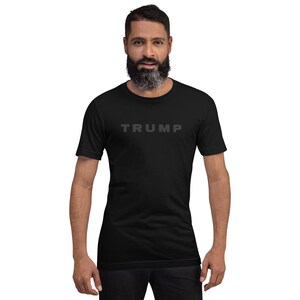 May include: A black t-shirt with the word "TRUMP" printed in gray on the front.