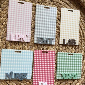 May include: A collection of six rectangular name badge holders with a gingham pattern in various colors: pink, gray, yellow, blue, red, and green. Each badge has a different profession title: LPN, EMT, LAB, Nurse, PA, and XRAY.