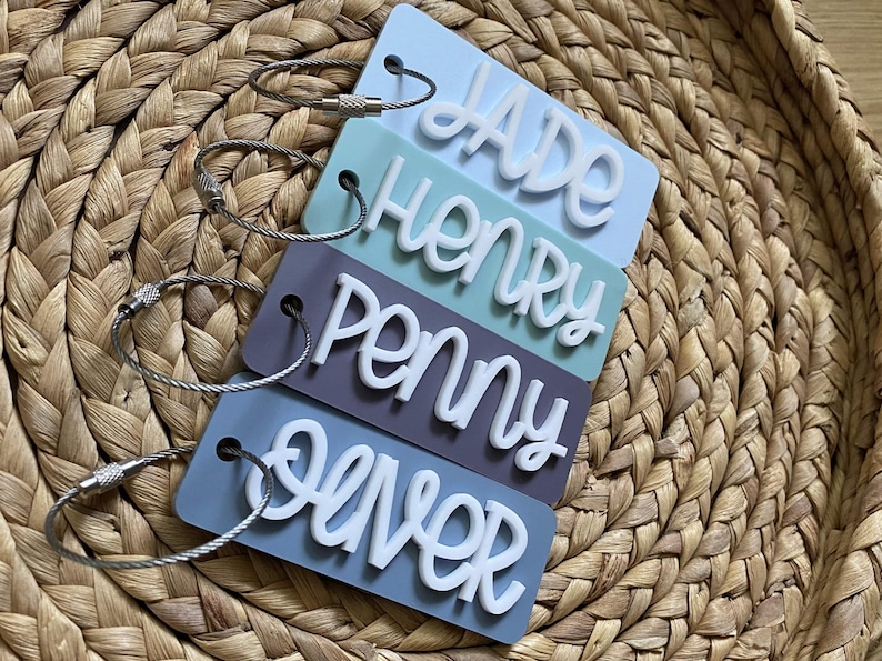 Peut inclure: Quatre &eacute;tiquettes &agrave; bagages de couleur pastel avec des lettres blanches. Les &eacute;tiquettes indiquent "Jade", "Henry", "Penny" et "Oliver". Chaque &eacute;tiquette est munie d'une boucle en m&eacute;tal argent&eacute;.