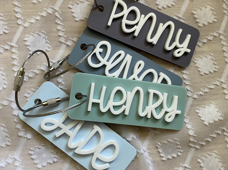 Peut inclure: Quatre porte-cl&eacute;s avec des noms diff&eacute;rents. Les noms sont "Penny", "Oliver", "Henry" et "Ade". Les porte-cl&eacute;s sont en acrylique bleu clair et gris avec des lettres blanches. Les porte-cl&eacute;s sont attach&eacute;s &agrave; des anneaux de cl&eacute;s en m&eacute;tal argent&eacute;.