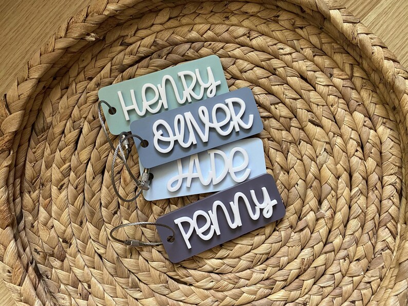 Peut inclure: Quatre porte-cl&eacute;s color&eacute;s avec des noms &eacute;crits en blanc dessus. Les noms sont Henry, Oliver, Jade et Penny. Les porte-cl&eacute;s sont sur un panier en osier.