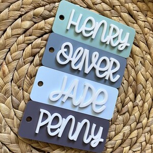 Peut inclure: Quatre porte-cl&eacute;s rectangulaires en acrylique avec des noms diff&eacute;rents &eacute;crits en lettres cursives blanches. Les noms sont Henry, Oliver, Jade et Penny. Les porte-cl&eacute;s sont dans des tons de bleu et de gris.